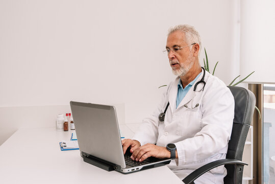 Aged man working with laptop in medical office