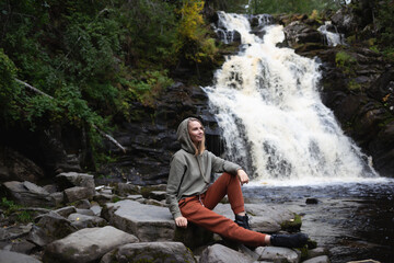a young beautiful woman tourist sitting against the backdrop of a waterfall surrounded by forest