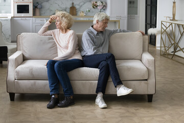 Angry frustrated tired senior couple sitting separately on home couch in silence, looking away, ignoring, thinking over relationship problems, divorce, breakup, marriage crisis - obrazy, fototapety, plakaty