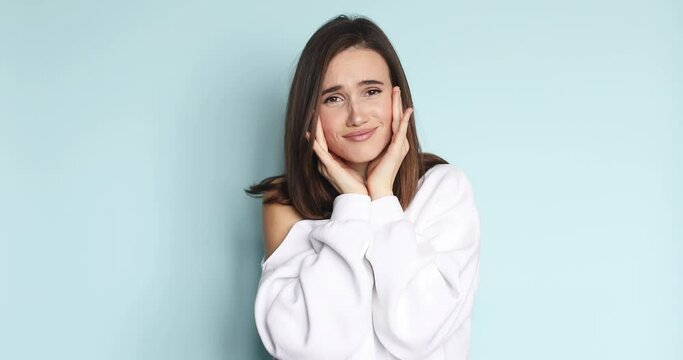 Brunette straight hair woman looking at camera charming smile, say oh it so sweet put hands on face. Girl wear white pullover isolated on blue background. Oh so sweet, so cute.