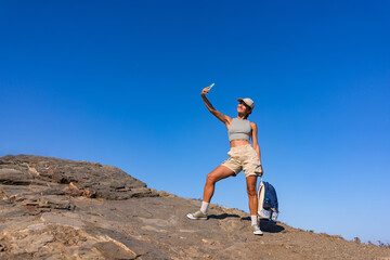 tourist girl with a backpack in the summer on top of a mountain takes a selfie against the backdrop of the sea and mountains