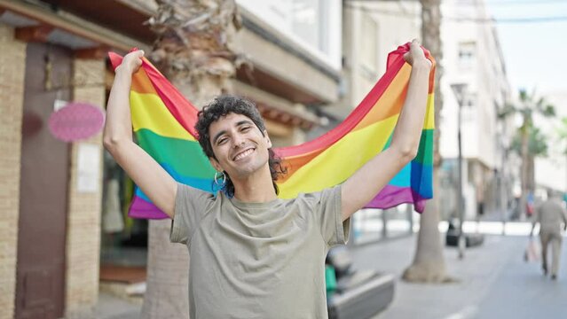 Young hispanic man smiling confident holding rainbow flag at street