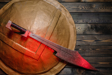 Ancient Spartan sword and shield on the wooden table background concept. Top view.