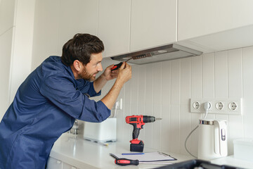 Professional male worker in uniform use screwdriver to repairing modern cooker hood in kitchen