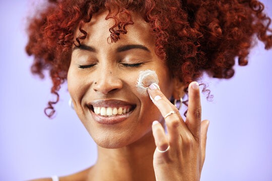 Beauty, skincare or happy woman with face lotion or sunscreen creme product in grooming routine. Dermatology cosmetics, purple background or biracial model with smile to apply facial cream in studio - Powered by Adobe