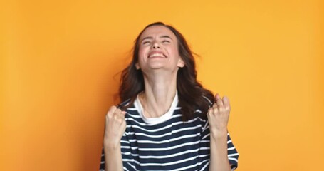 Overjoyed curly haired woman wins competition achieves goal and makes triumph gesture says yes feels like winner shows fist bump happy dream come true poses against yellow background.
