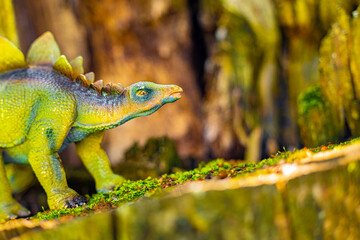 a toy dinosaur walks on a mountain overgrown with grass