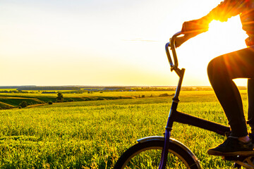 Naklejka premium woman riding a bike through a field at sunset.