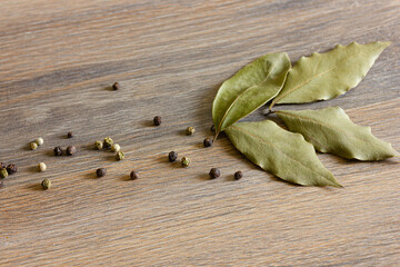 Peppercorns and bay leaves are scattered on a wooden table.