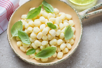 Beige serving pan with uncooked potato gnocchi and fresh green basil, horizontal shot, middle closeup
