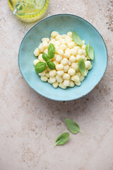 Blue bowl with raw italian gnocchi or chicche di patate on a beige stone background, vertical shot with space, above view