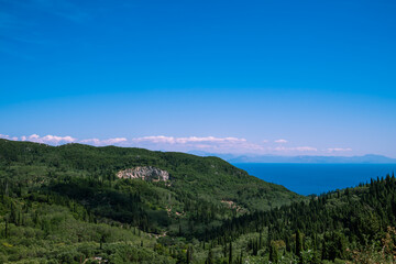 Scenic top view of the green slopes of the mountains and the sea on a clear sunny day.