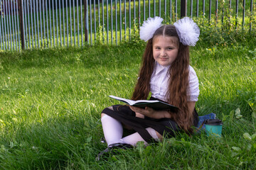 A happy girl with bows on her hair is sitting on the grass and reading a book