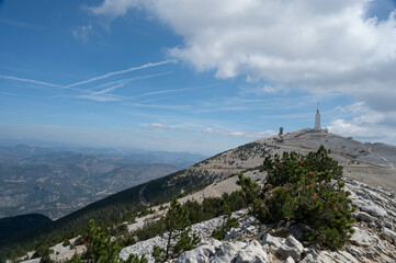 The top of the Mont Ventoux in Vaucluse at 1910m.  The observation tower is on the right of the picture. A blue and cloudy sky. Trees in the foreground.
