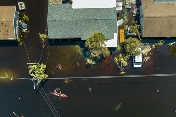 Aftermath of flooding natural disaster. Kayak boat floating on flooded street surrounded by...