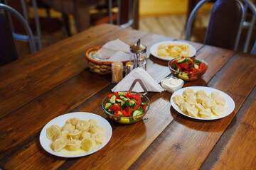 Wooden table with plates with simple dishes. dumplings and salad