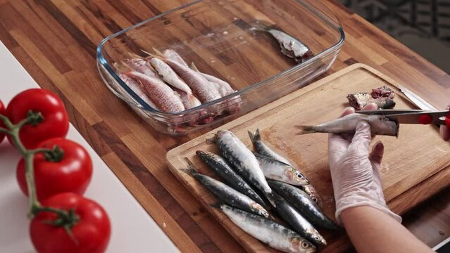 Close-up view of housewife hands cleaning fish on a wooden cutting board. Cooking small sardines, real time