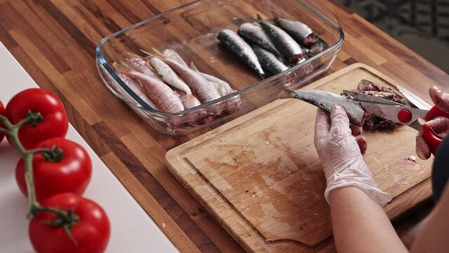 Close-up view of housewife hands cleaning fish on a wooden cutting board. Cooking small sardines, real time