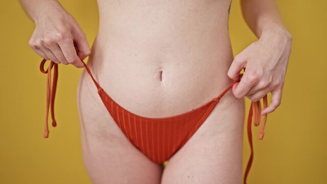 Young blonde woman tourist wearing bikini dancing over isolated yellow background
