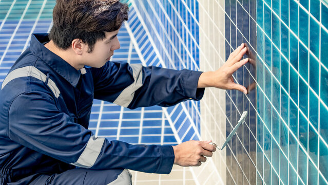 Asian Man Construction Worker Using Trowel Or Building Spatula Spreading Cement Grout On Blue Ceramic Tiles In The Swimming Pool