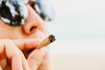 Young man smoking drug medical cannabis, weed at the beach.