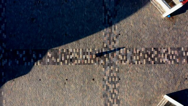 Persona silueta caminando sobre mosaicos de texturas en el piso en el camino en la calle proyectando una sombra sobre la explanada en un d&iacute;a soleado en la vereda con piedras paisaje sombreado 