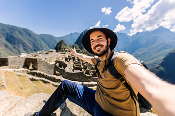 Happy young adult man taking selfie portrait in Machu Picchu. Joyful traveler enjoying vacation visiting Peru. South american travel holidays concept. - obrazy, fototapety, plakaty
