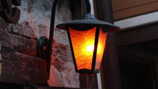 outdoor medieval metal lantern with a warm candle inside the glass with a flame burning and a stone wall in the background. Medieval environment ambient for a fairy tale in an old town