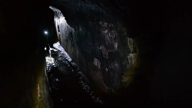 Digger person walking through dark tunnel adit, rain collector, sewer tunnel underground, illuminating light of lantern flashlight. Infrastructure of mine adit for underground river. Sewage collector