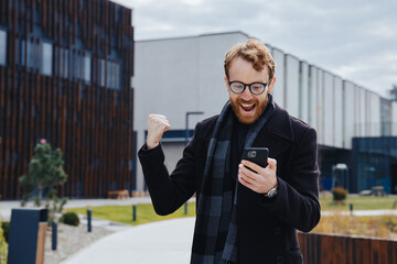 A young red-haired guy, a businessman in glasses, against the backdrop of an urban style, makes...