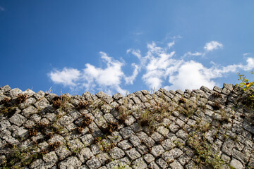 Old ruins roman stone wall against a blue sky,  stonefaced wall with green leaves on an overgrown. Ancient Roman brick wall covered with grass and clouds. Riuns and cultural heritage background.
