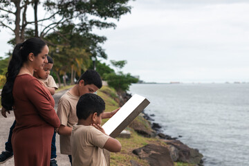 latino family standing with their backs to each other reading a sign at the seaside