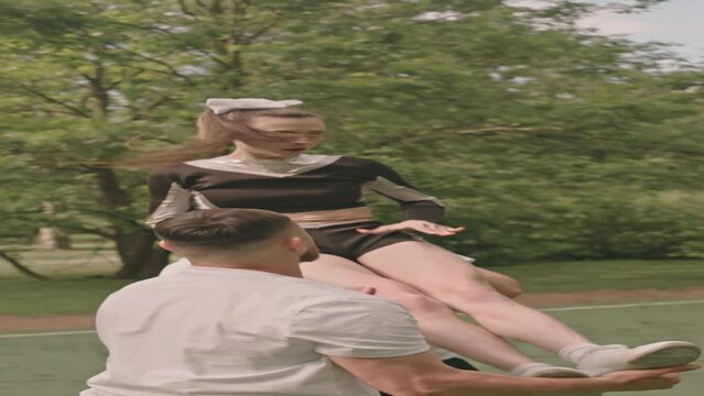 Vertical shot of flyer girl performing stunt with two male partners while training together on football field outdoors