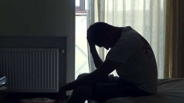 Silhouette of depressed man sitting on a floor. Sad unhappy person in a bedroom thinking about something
