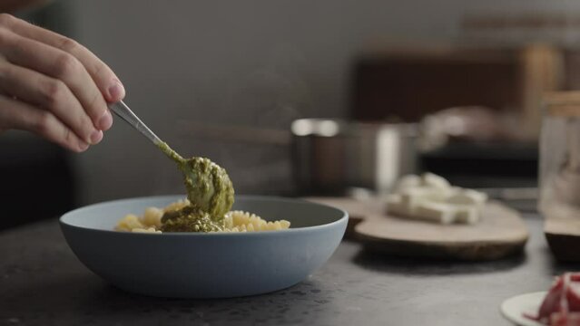 Slow motion add pesto sauce to fusilli pasta in blue bowl