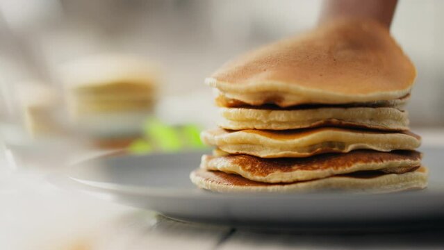 Syrup. A stay-at-home parent stacks a pile of pancakes on a plate in a home kitchen. General perspective modern mom stacks a pile of pancakes on a plate new methods of preparing fresh breakfast, baked