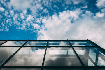 Transparent glass walls of office buildings. A modern office building with a glass facade against a cloudy sky. Glazed building with blue sky. The sky with clouds is reflected in the windows