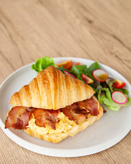 Croissant with scrambled egg, bacon and salad