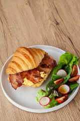 Croissant with scrambled egg, bacon and salad
