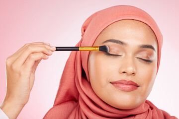 Beauty, makeup and muslim woman in studio with a brush for eyeshadow, glamour or face routine. Cosmetics, self care and young islamic female model with cosmetology product isolated by pink background