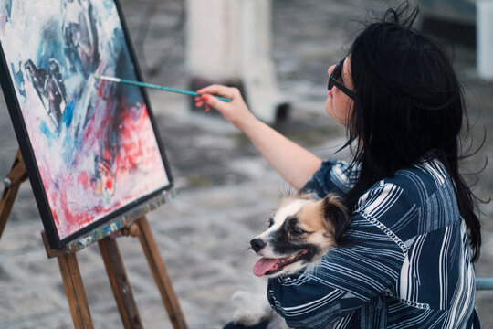A woman artist's portrait with her dog painting on a building rooftop