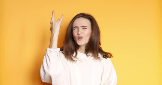 Carefree delighted beautiful girl scream woo and rock and roll hand gesture, punk sign, shouting excited by win. indoor studio shot isolated on yellow background
