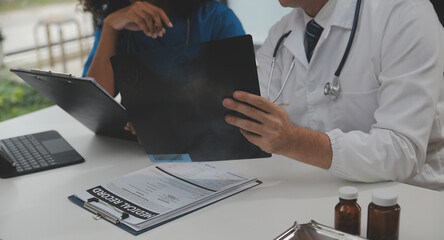 Focused mature male doctor and female nurse look at tablet screen discuss anamnesis together. Concentrated diverse medical professionals use pad device, engaged in team thinking in hospital. - obrazy, fototapety, plakaty