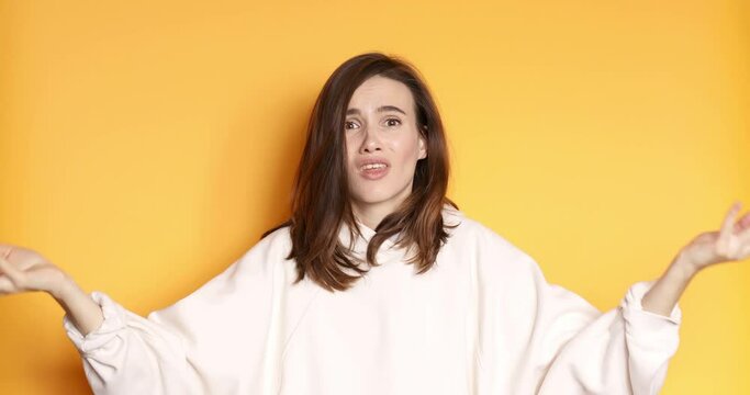 Woman asks why and spreads hands to the sides isolated on yellow background. Woman is perplexed and unknown. Concept of the question.