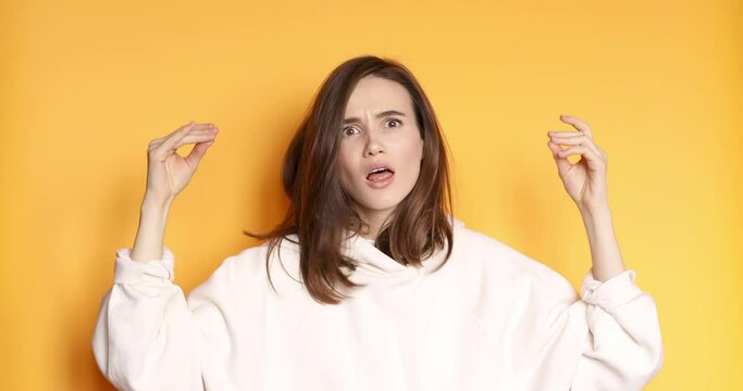 Brunette indignant woman wear white hoody showing bla bla bla gesture with hands isolated on studio yellow background. Empty promises, blah concept. Lier.