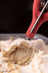Red handled ice cream scoop scooping a serving of caramel butterscotch ripple ice cream from container, copy space