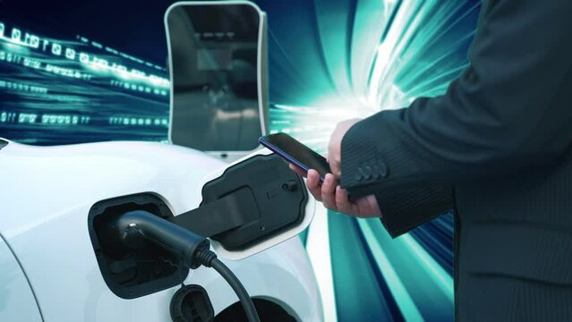 Progressive man check electric car's battery status with smartphone at charging station with technology background of binary code flying through votex. EV car concept with modern technology.