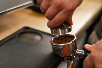 Fototapeta na wymiar Barista holding portafilter and coffee tamper making an espresso in cafe, close-up.