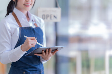 Asian  business woman in an apron, the owner of the cafe stands at the door with a sign Open waiting for customers , cafes and restaurants Small business concept.