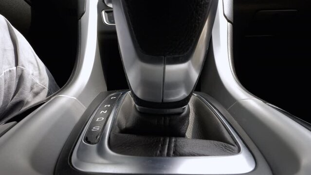 Driver's hand shifts car gear stick to sport drive mode. Shifting automatic transmission, close up